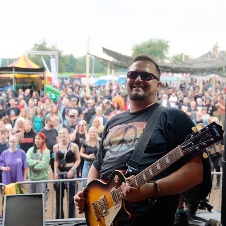Jaro, Gitarrist der Hot Tuesdays, strahlt während des Auftritts der Hot Tuesdays beim Südwinsen Festival 2023 in die Kamera des Fotografen